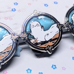 May include: Three enamel pins featuring a white cartoon creature with a blue background. The creature is depicted in different poses, with stars and a crescent moon in the background.