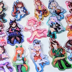 Könnte beinhalten: Eine Sammlung von Acryl-Anhängern mit Anime-Charakteren in verschiedenen Posen und Outfits. Die Anhänger zeigen lebendige Farben und detaillierte Designs, wobei jeder Charakter ein einzigartiges Aussehen hat. Die Anhänger sind transparent mit glänzendem Finish.