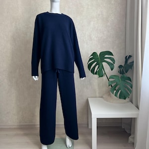 Op de afbeelding: Een donkerblauwe tweedelige loungeset bestaande uit een trui met lange mouwen en een ronde hals en een bijpassende broek met wijde pijpen. De trui heeft geribbelde boorden en een geribbelde zoom, terwijl de broek een taille met trekkoord heeft.