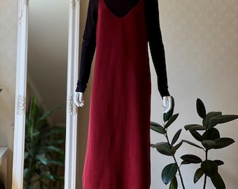 May include: A burgundy-colored slip dress with a V-neck, layered over a black long-sleeved turtleneck. The dress is displayed on a mannequin. A white framed mirror and a potted plant are in the background.