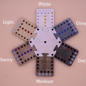 May include: A set of seven wooden game boards in different shades of brown, from white to dark, with white dots around the edges and colored dots in the center. The boards are arranged in a circle, with the lightest board at the top and the darkest board at the bottom. The boards are labeled with the color names: White, Light, Cherry, Medium, Dark, Gray.