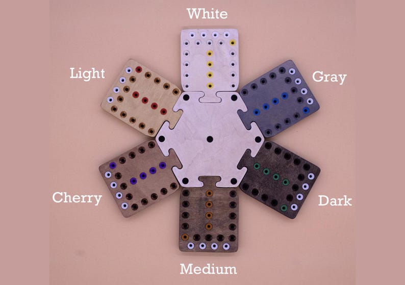 May include: A set of seven wooden game boards in different shades of brown, from white to dark, with white dots around the edges and colored dots in the center. The boards are arranged in a circle, with the lightest board at the top and the darkest board at the bottom. The boards are labeled with the color names: White, Light, Cherry, Medium, Dark, Gray.