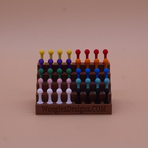 May include: A display stand with a variety of colorful, round-topped, plastic pegs. The stand is made of brown plastic and has the text "WoogiezDezignaz.COM" printed on the front.