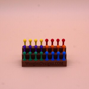 May include: A wooden stand with a rainbow of colored pegs. The stand has three tiers and is labeled "WoogiezDezignaz.COM".