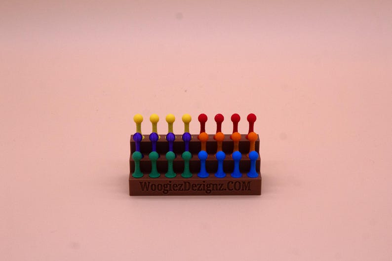May include: A wooden stand with a rainbow of colored pegs. The stand has three tiers and is labeled "WoogiezDezignaz.COM".