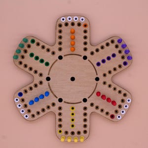 May include: A wooden game board shaped like a flower with six points. Each point has a track of holes with colored pegs in them. The colors of the pegs are white, orange, red, blue, green, and yellow.