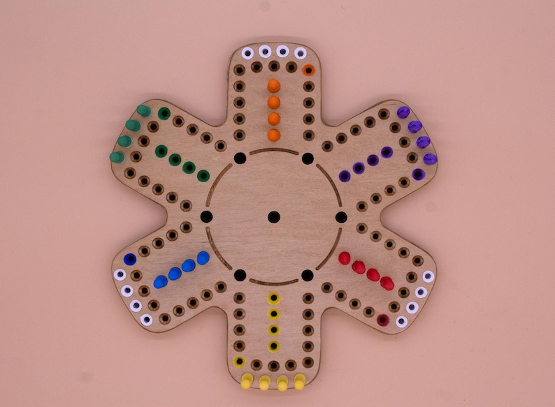 May include: A wooden game board shaped like a flower with six points. Each point has a track of holes with colored pegs in them. The colors of the pegs are white, orange, red, blue, green, and yellow.