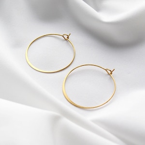 Op de afbeelding: Een paar gouden creolen op een witte stoffen achtergrond.