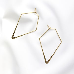 Op de afbeelding: Een paar gouden geometrische creolen. De oorbellen zijn diamantvormig en hebben een eenvoudig, modern ontwerp.