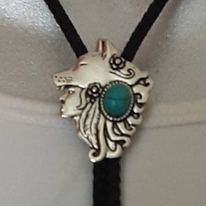 May include: A silver bolo tie featuring a wolf's head design with a turquoise stone.