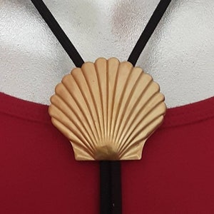 Könnte beinhalten: Ein goldener Muschelanhänger an einer schwarzen Schnurkette. Die Muschel ist ein dekorativer Akzent für ein Schmuckstück.