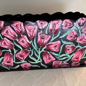 May include: Black metal planter with a scalloped rim, painted with pink tulips and green leaves.