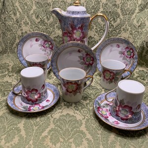May include: A vintage floral tea set with a teapot, cups, and saucers. The set features a blue and white background with pink and red floral designs and gold accents.