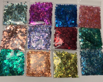 May include: Twelve small bags of iridescent glitter shaped like butterflies. The bags are arranged in four rows of three. The glitter colors are teal, pink, blue, red, gold, brown, purple, green, and orange.