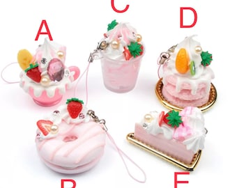 May include: Five pink and white dessert-themed charms with a gold accent. The charms are shaped like a cupcake, a donut, a parfait, a cake, and a slice of cake. Each charm has a small strawberry, whipped cream, and other decorative elements.