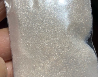 May include: A clear plastic bag filled with iridescent white glitter. The bag has a label that says "10g".