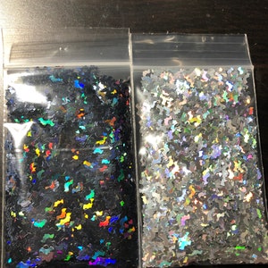 May include: Two small bags of iridescent glitter shaped like bats. One bag is black with rainbow iridescent glitter and the other bag is silver with rainbow iridescent glitter.