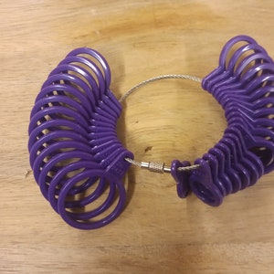 May include: A purple plastic ring sizer with a metal chain connecting the two halves. The sizer has a range of sizes from 4 to 13.