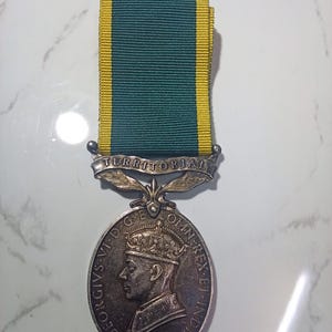 May include: A silver Territorial Efficiency Medal with a green and yellow striped ribbon. The medal features a profile of a crowned figure and the inscription "GEORGIVS VI D:G:BR:OMN:REX ET INDIA:IMP". The word "TERRITORIAL" is inscribed above the medal.