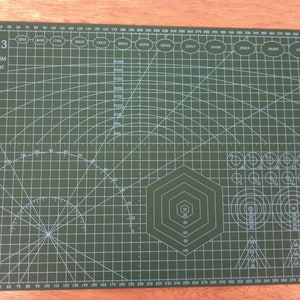 May include: Dark green A3 cutting mat, measuring 450 x 300mm (17.7 x 11.8 inches). It has grid lines, angles, circles, and a hexagon shape. Includes measurements in millimetres.
