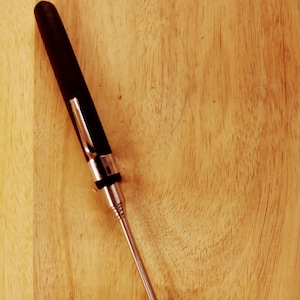 May include: A black and silver telescopic magnetic pick-up tool with a round tip. The tool is lying on a wooden surface.