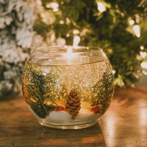 shalant clear gel candles: Pine and snow candles made with pine garland pine cones and sugar snow in clear gel wax. jelly candle in a glass cup. These candles have a refillable glass votive in the center. Gel wax is scented with a pine balsam scent