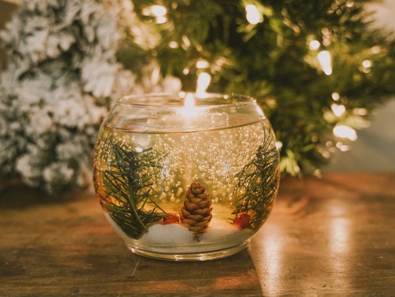 shalant clear gel candles: Pine and snow candles made with pine garland pine cones and sugar snow in clear gel wax. jelly candle in a glass cup. These candles have a refillable glass votive in the center. Gel wax is scented with a pine balsam scent