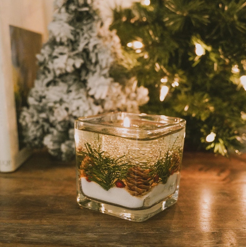 shalant holiday gel candles Pine and snow candles made with pine garland pine cones and sugar snow in clear gel wax. jelly candle in a glass cube. These candles have a refillable glass votive in the center. Gel wax is scented with a pine balsam scent