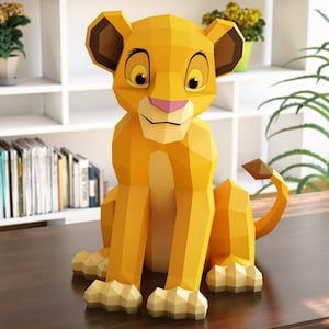 May include: A yellow geometric papercraft lion figurine with brown ears, a pink nose, and a curled tail. The lion is sitting on a dark brown surface. The figurine is a 3D paper art sculpture.