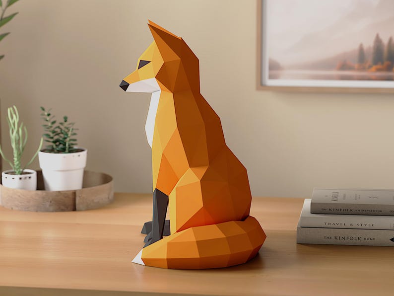 Pode incluir: Uma escultura geom&eacute;trica de raposa laranja com detalhes em preto. A raposa de papel est&aacute; sentada, com a cauda enrolada. A escultura est&aacute; sobre uma superf&iacute;cie de madeira, com plantas e livros ao fundo.