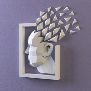 K&ouml;nnte beinhalten: Ein wei&szlig;es, geometrisches Wandkunstwerk, das einen menschlichen Kopf in einem rechteckigen Rahmen darstellt. Der Kopf besteht aus winkligen Ebenen, wobei dreieckige Formen von oben ausgehen und Gedanken oder Ideen andeuten. Das Kunstwerk ist an einer lila Wand angebracht.