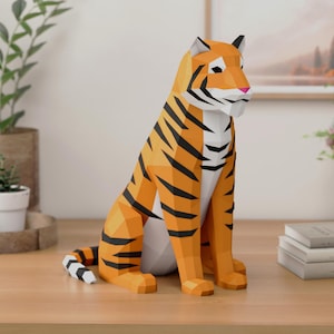 Puede incluir: Una escultura de tigre de papel low-poly con un diseño geométrico de paneles naranjas, negros y blancos. El tigre está representado en posición sentada con la cola curvada hacia un lado, mostrando facetas angulares y una forma estilizada.