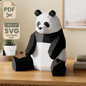 Peut inclure: Une sculpture géométrique d'un panda noir et blanc est posée sur une surface en bois. Le panda est fait de papier plié ou de carton. L'image comprend également le texte "PDF" et "CRICUT SVG CUT READY FILES".