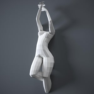 May include: A white, geometric wall sculpture of a human form in a graceful pose, with arms raised overhead. The sculpture is mounted on a gray wall, creating a striking contrast. The figure's form is composed of angular planes.