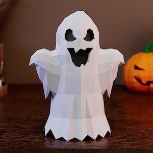 May include: A white, low-poly ghost figurine with a geometric, faceted surface. The ghost features large, dark, triangular eye cutouts and a jagged, open-mouthed expression, creating a stylised, angular appearance with a scalloped bottom edge.
