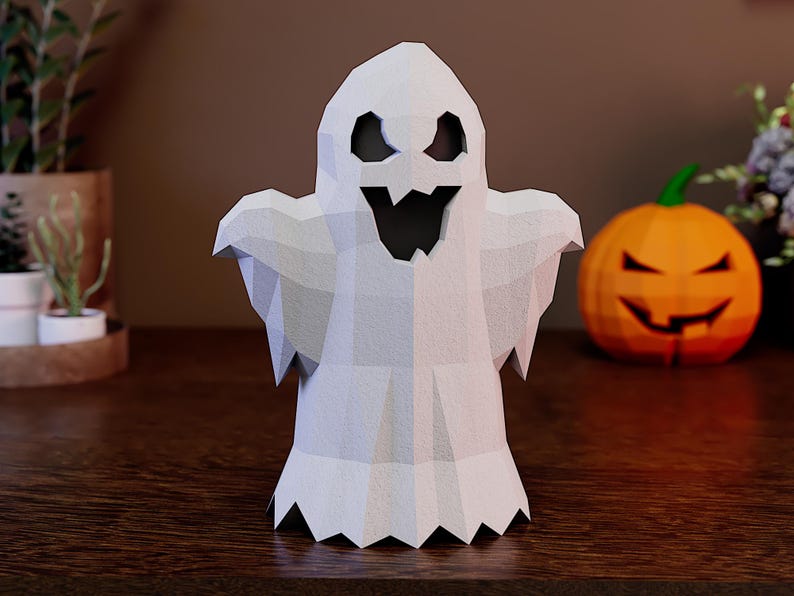 May include: A white, low-poly ghost figurine with a geometric, faceted surface. The ghost features large, dark, triangular eye cutouts and a jagged, open-mouthed expression, creating a stylized, angular appearance with a scalloped bottom edge.
