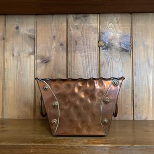 May include: A hammered copper planter with two handles. The planter has a scalloped edge and is a warm copper colour.