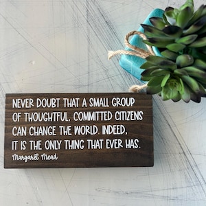 May include: A wooden sign with a quote by Margaret Mead: "Never doubt that a small group of thoughtful, committed citizens can change the world. Indeed, it is the only thing that ever has."