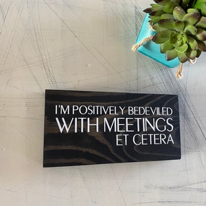 May include: A black wooden sign with white text that reads "I'm positively bedeviled with meetings et cetera".