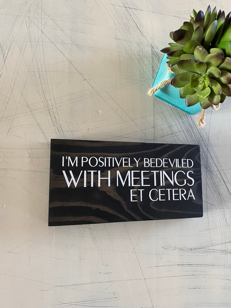 May include: A black wooden sign with white text that reads "I'm positively bedeviled with meetings et cetera".