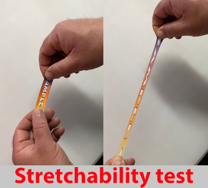 Pode incluir: Um adesivo retangular, colorido e extens&iacute;vel com a palavra "SAMPLE" impressa nele. O adesivo est&aacute; sendo esticado para mostrar sua flexibilidade.