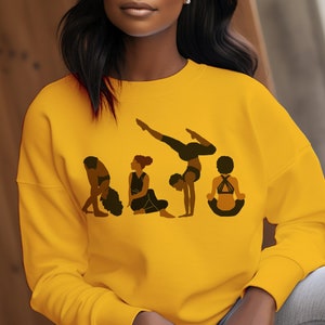 May include: A yellow sweatshirt with a graphic of five women in different yoga poses. The women are all black and the poses are varied, including a handstand, a seated pose, and a forward bend.
