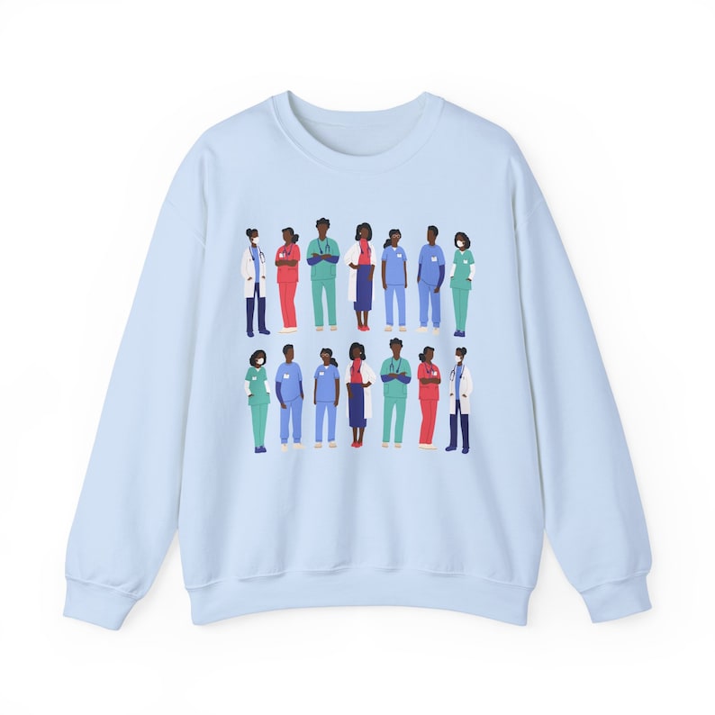 May include: Light blue sweatshirt with a graphic print of a group of diverse healthcare workers wearing scrubs and face masks.