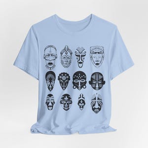 May include: A light blue t-shirt with a pattern of black and white African masks. The masks are arranged in a grid pattern on the front of the shirt.