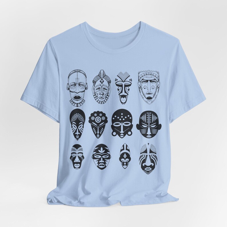 May include: A light blue t-shirt with a pattern of black and white African masks. The masks are arranged in a grid pattern on the front of the shirt.