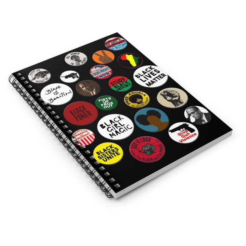 May include: Black and white spiral notebook with colorful button pins featuring slogans like "Black is Beautiful", "Black Power", "Black Girl Magic", "Black Lives Matter", and "Black Sisters Unite".