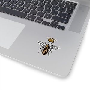 Puede incluir: Una abeja negra y amarilla con una corona dorada en la cabeza. La abeja est&aacute; en posici&oacute;n de vuelo con las alas extendidas.