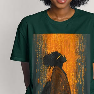 May include: Dark green t-shirt featuring a silhouette of a person wearing sunglasses, looking upwards. The graphic has a matrix-like background with yellow and orange tones. The shirt is made of a soft material.