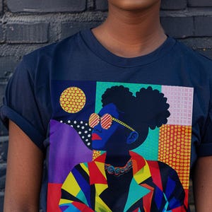 May include: A navy blue t-shirt featuring a colourful graphic print of a woman wearing sunglasses. The graphic incorporates geometric shapes and patterns in shades of blue, red, yellow, green, and purple.