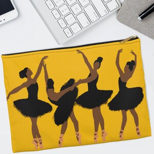 Pode incluir: Uma bolsa amarela com z&iacute;per com um gr&aacute;fico de quatro bailarinas de bal&eacute; em tutus pretos e sapatilhas de ponta rosa. As bailarinas s&atilde;o retratadas em v&aacute;rias poses graciosas em um fundo amarelo s&oacute;lido. A bolsa tem um z&iacute;per dourado.